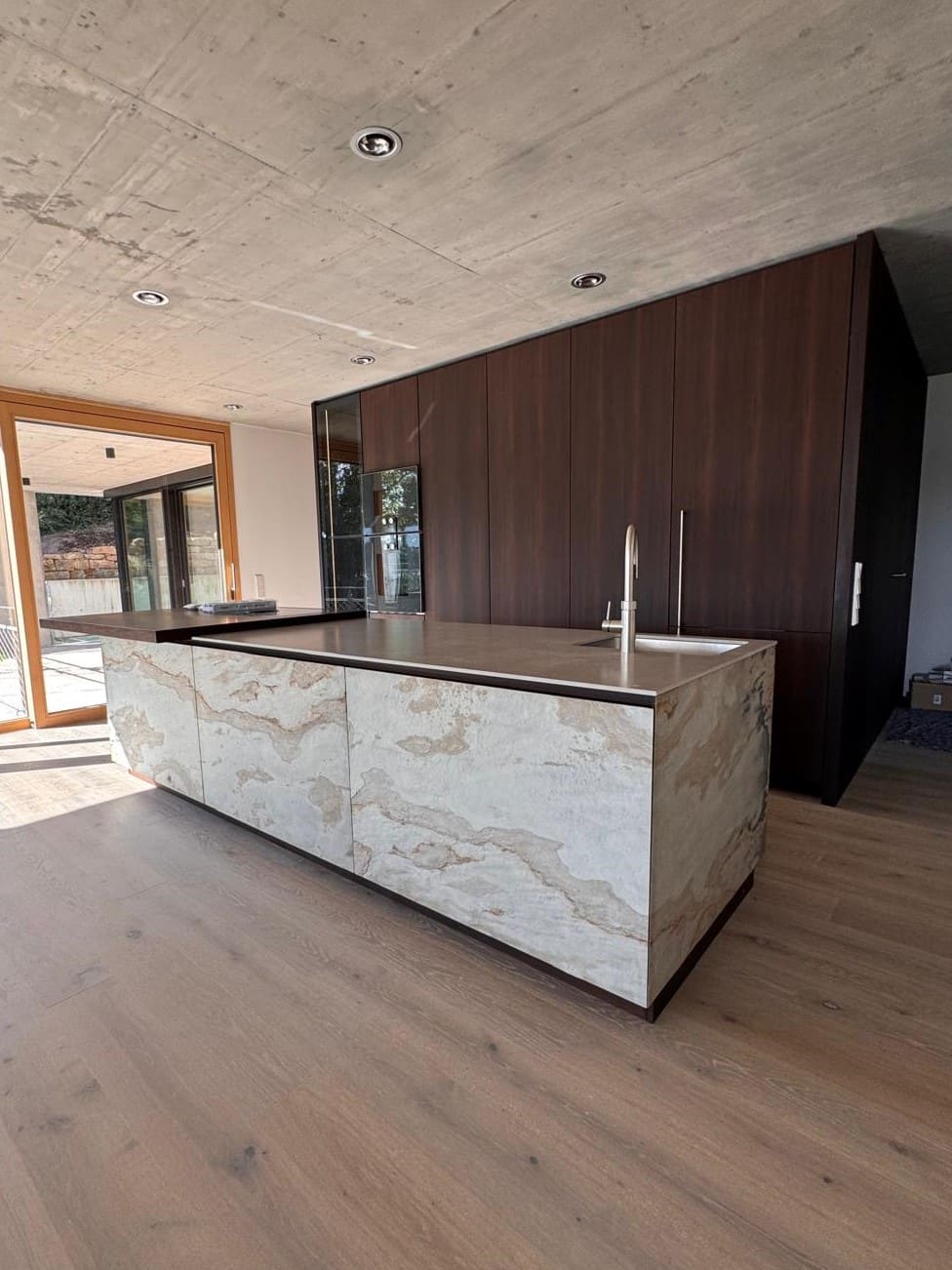 Designküche, Natursteinfronten und dunkles Holz, integrierte Geräte.